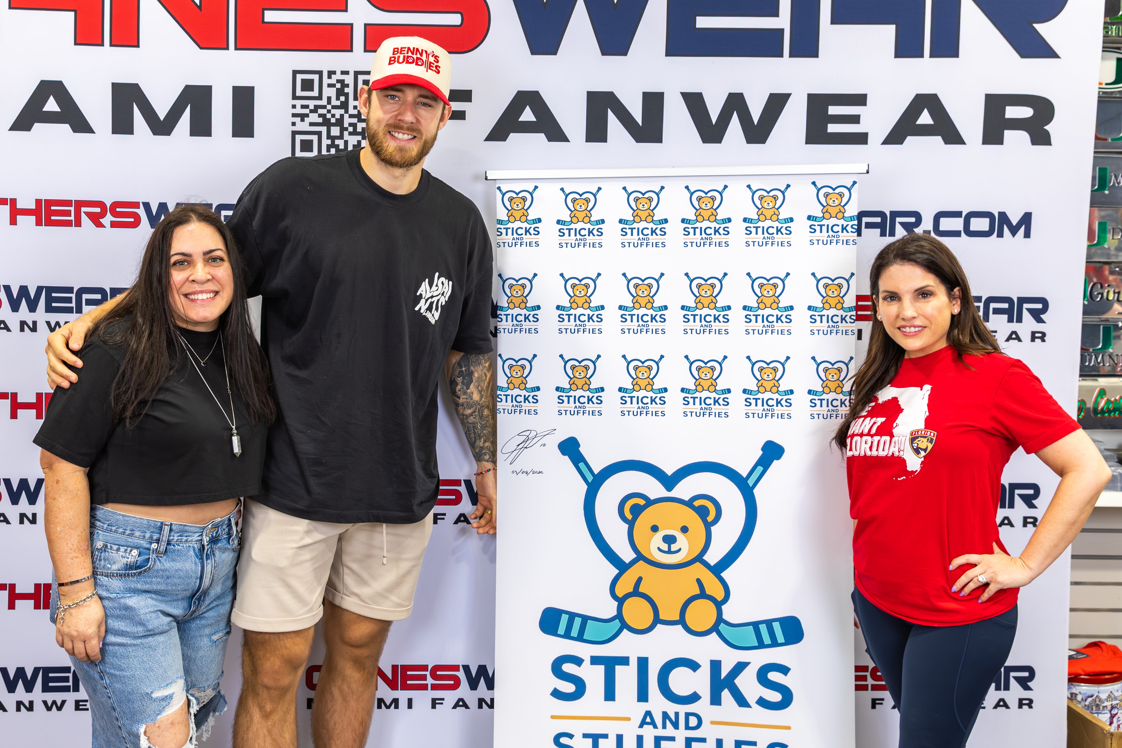 A.J. Greer with two fans in front of the Sticks and Stuffies backdrop at CanesWear